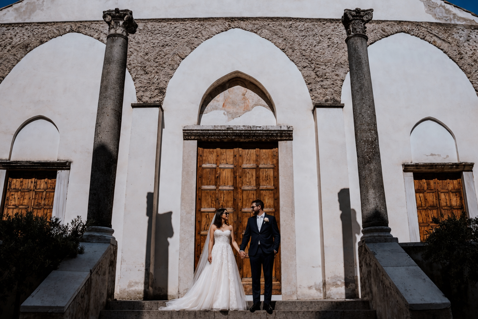 newlywed couple standing in front of church entrance in Ravello with columns and wooden doors