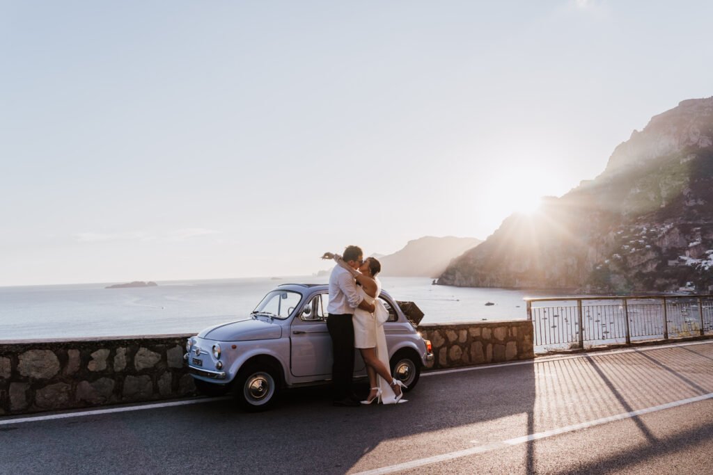 Couple kissing by a vintage car in Positano during a romantic sunset photo session on the Amalfi Coast